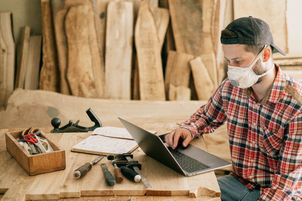 Woodworker wearing mask using laptop in workshop creating a template website
